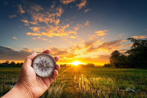 A,Man,Holding,Compass,On,Hand,At,Field,And,Sunset